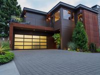 the driveway of this large home has black brick pavers in it, and lights are on