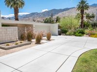 a driveway leading into a home with palm trees in the background and mountains beyond the driveway