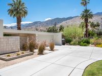 a driveway leading into a home with palm trees in the background and mountains beyond the driveway