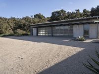 a house that has gravel flooring around it outside, with an open garage and a grassy lawn in front