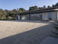 a house that has gravel flooring around it outside, with an open garage and a grassy lawn in front