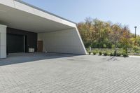 the front of the building shows a paved stone driveway and side entrance, with multiple garage doors and trees in the distance