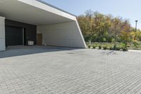 the front of the building shows a paved stone driveway and side entrance, with multiple garage doors and trees in the distance