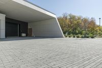 the front of the building shows a paved stone driveway and side entrance, with multiple garage doors and trees in the distance