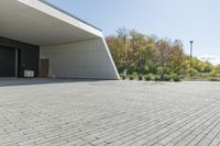 the front of the building shows a paved stone driveway and side entrance, with multiple garage doors and trees in the distance