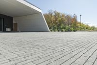 the front of the building shows a paved stone driveway and side entrance, with multiple garage doors and trees in the distance