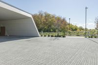 the front of the building shows a paved stone driveway and side entrance, with multiple garage doors and trees in the distance