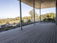 the covered deck area with the view to the outdoors area of the house and forest in the distance