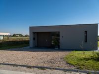 a house sitting on top of a gravel field next to a road of grass and bushes