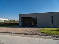 a house sitting on top of a gravel field next to a road of grass and bushes