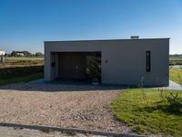 a house sitting on top of a gravel field next to a road of grass and bushes