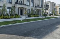 a lone person rides a bike down the road between two row homes and green grass