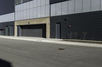 there is a person standing outside of an industrial building with a large black door in the middle of a street