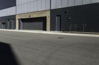 there is a person standing outside of an industrial building with a large black door in the middle of a street