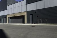 there is a person standing outside of an industrial building with a large black door in the middle of a street