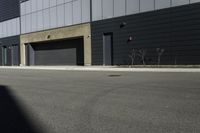 there is a person standing outside of an industrial building with a large black door in the middle of a street