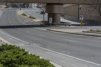 an empty street under a bridge in the cityscape with shrubs and green bushes