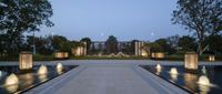 several fountains in a row with trees and a sky background at twilight behind them near some white lights