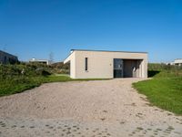 a gravel driveway leading to a white building on the right side of the driveway that has a car door open