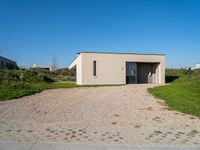 a gravel driveway leading to a white building on the right side of the driveway that has a car door open