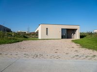 a gravel driveway leading to a white building on the right side of the driveway that has a car door open