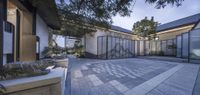 a very beautiful courtyard area with white brick paving and lots of trees and bushes surrounding the entrance