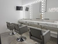 an empty modern salon with mirrors, lights, and a television on the wall as well as many chairs