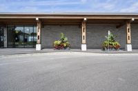 a stone building on the left side with a sidewalk to right and a parking lot area in front