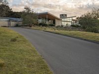 a street view looking towards a modern style building, which sits against a hill and surrounded by trees and a grass covered area