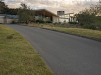 a street view looking towards a modern style building, which sits against a hill and surrounded by trees and a grass covered area