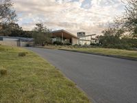 a street view looking towards a modern style building, which sits against a hill and surrounded by trees and a grass covered area