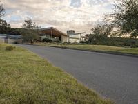 a street view looking towards a modern style building, which sits against a hill and surrounded by trees and a grass covered area