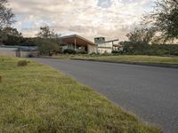 a street view looking towards a modern style building, which sits against a hill and surrounded by trees and a grass covered area