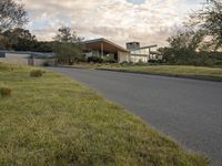 a street view looking towards a modern style building, which sits against a hill and surrounded by trees and a grass covered area