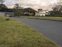 a street view looking towards a modern style building, which sits against a hill and surrounded by trees and a grass covered area