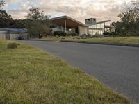 a street view looking towards a modern style building, which sits against a hill and surrounded by trees and a grass covered area