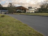 a street view looking towards a modern style building, which sits against a hill and surrounded by trees and a grass covered area