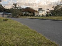 a street view looking towards a modern style building, which sits against a hill and surrounded by trees and a grass covered area