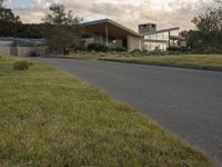 a street view looking towards a modern style building, which sits against a hill and surrounded by trees and a grass covered area