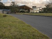 a street view looking towards a modern style building, which sits against a hill and surrounded by trees and a grass covered area