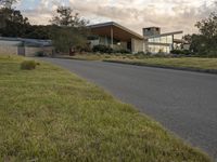 a street view looking towards a modern style building, which sits against a hill and surrounded by trees and a grass covered area