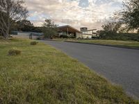 a street view looking towards a modern style building, which sits against a hill and surrounded by trees and a grass covered area