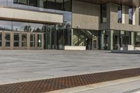 a modern style building with glass walls and entrance and sidewalk, and a few benches sitting on the front side, and in front of it