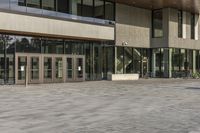 a modern style building with glass walls and entrance and sidewalk, and a few benches sitting on the front side, and in front of it