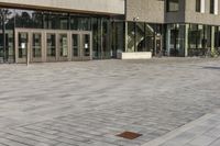 a modern style building with glass walls and entrance and sidewalk, and a few benches sitting on the front side, and in front of it