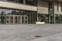 a modern style building with glass walls and entrance and sidewalk, and a few benches sitting on the front side, and in front of it