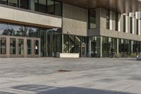 a modern style building with glass walls and entrance and sidewalk, and a few benches sitting on the front side, and in front of it