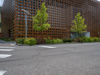 street corner with tree on the corner of the corner and a building behind it that is surrounded by multiple windows and a perforated brown lattice