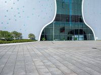 a white building with polka dots on the side of it is glassy windows and has a small green potted plant on the floor near a brick pathway