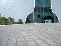 a white building with polka dots on the side of it is glassy windows and has a small green potted plant on the floor near a brick pathway